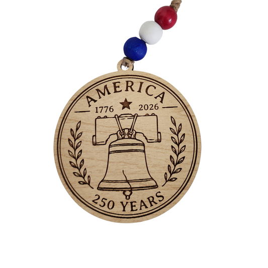 Handcrafted wooden America 250 ornament featuring Liberty Bell. Laser engraved patriotic keepsake with red, white, and blue bead accents celebrating America's 250th anniversary.