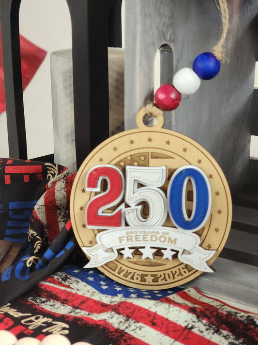 Handcrafted 250 Years of Freedom ornament made from layered maple wood with red, white, and blue raised lettering, engraved patriotic details, jute hanger, and patriotic wood beads celebrating America's 250th birthday.