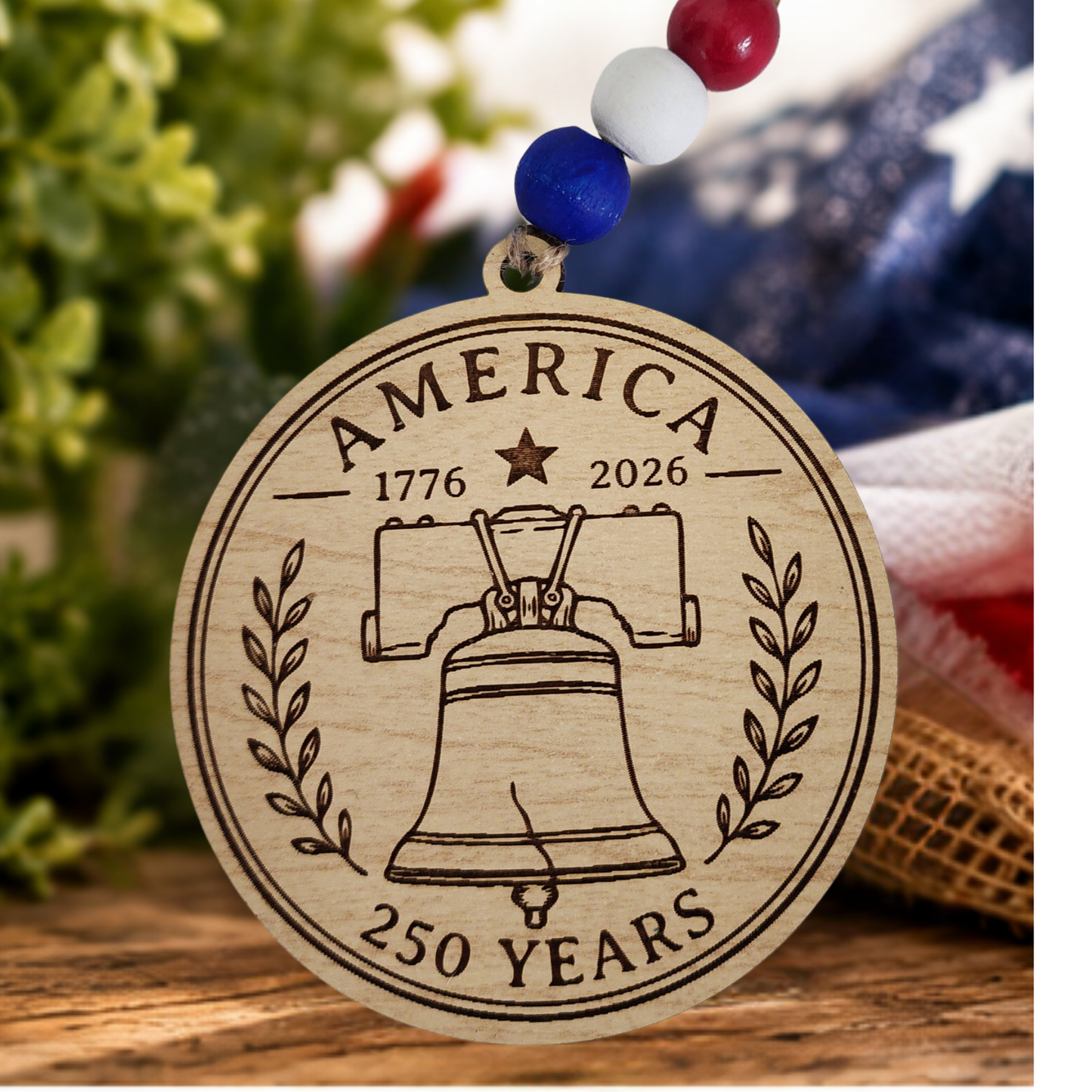 Handcrafted wooden America 250 ornament featuring Liberty Bell. Laser engraved patriotic keepsake with red, white, and blue bead accents celebrating America's 250th anniversary.